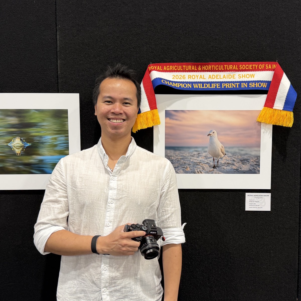 Ricky Vu holding the Champion Wildlife Print in Show ribbon beside his award-winning photograph at the 2026 Royal Adelaide Show